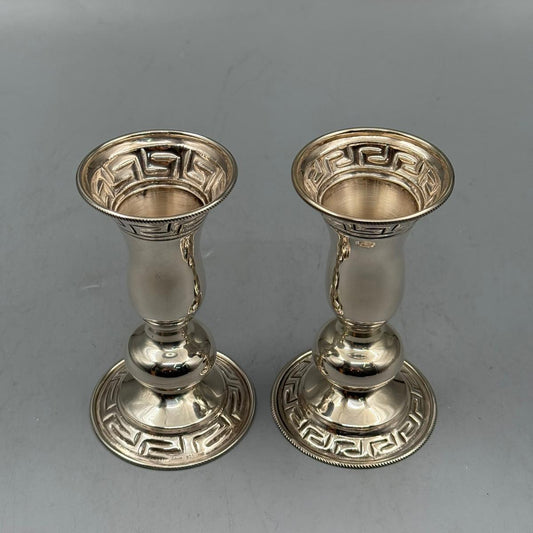 Pair of silver candle holders with Greek key design, viewed from above.