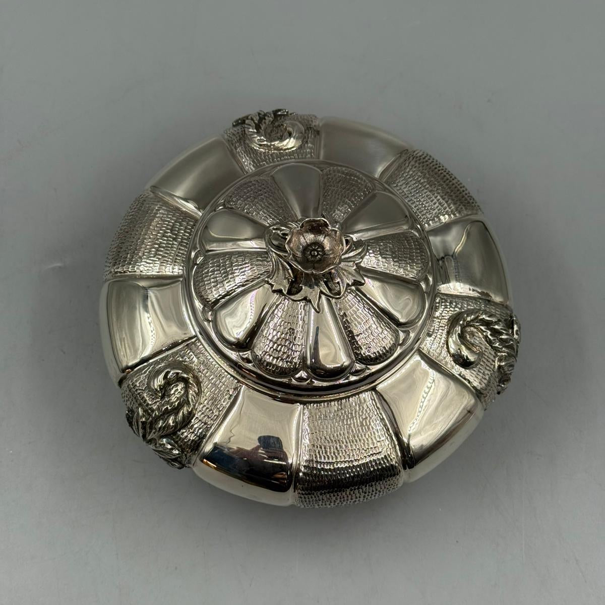 Silver round box with an open lid showing inner compartment and floral exterior details.