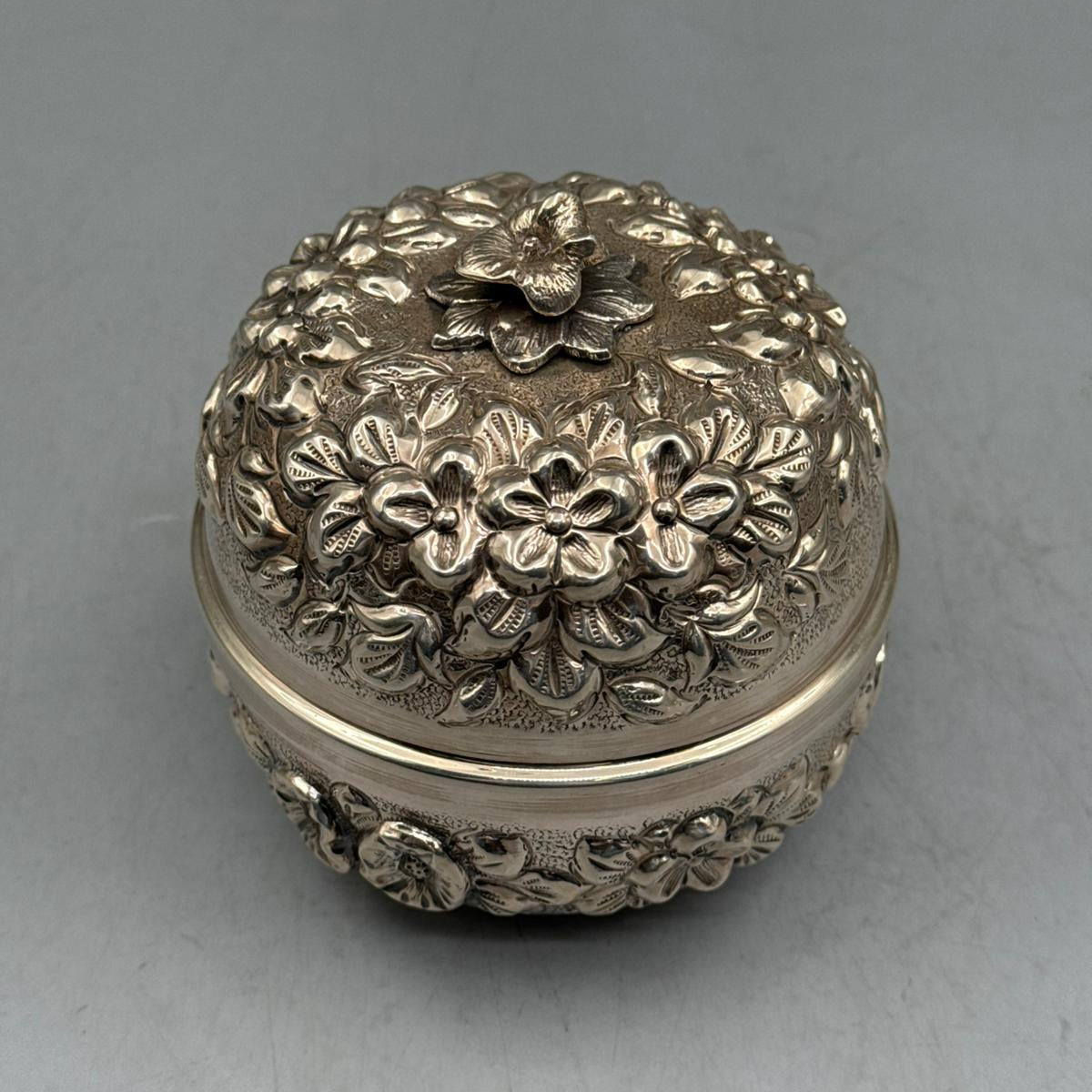 Top-down view of the meticulously hand-chased floral patterns and the sculpted silver flower handle on the sterling silver lid.
