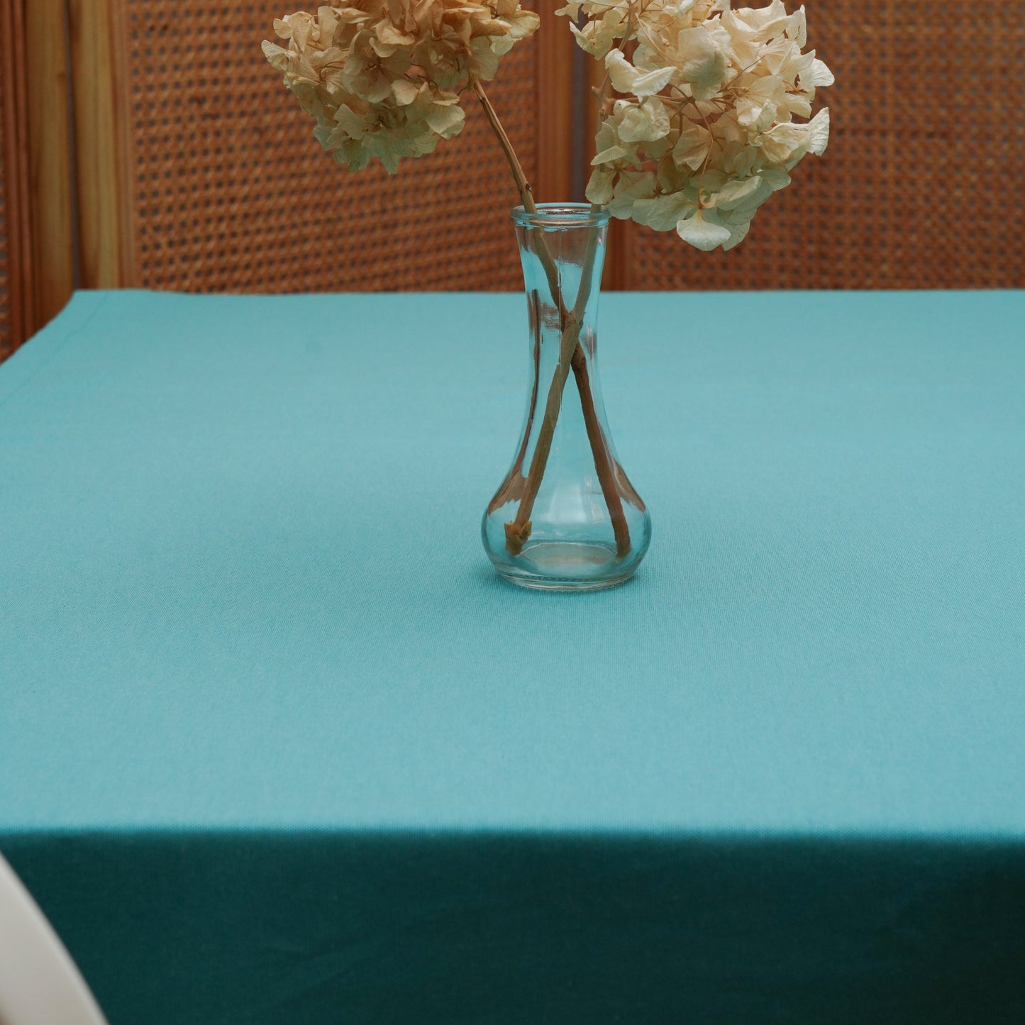 Teal aqua rectangular tablecloth styled with a clear glass vase and dried hydrangeas in a warm dining setting
