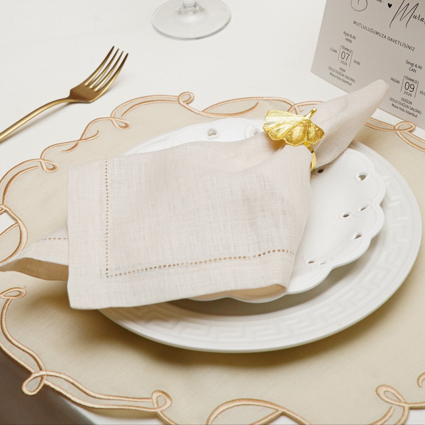 A close-up of an elegant white cloth napkin featuring a custom navy blue embroidered initial W within a decorative crest, presented as a high-quality gift option for hostesses.