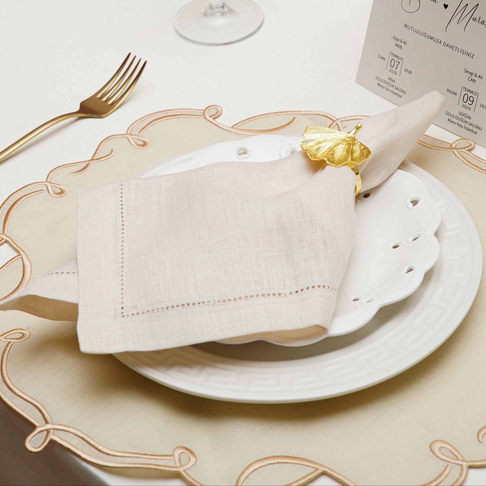A close-up of an elegant white cloth napkin featuring a custom navy blue embroidered initial W within a decorative crest, presented as a high-quality gift option for hostesses.