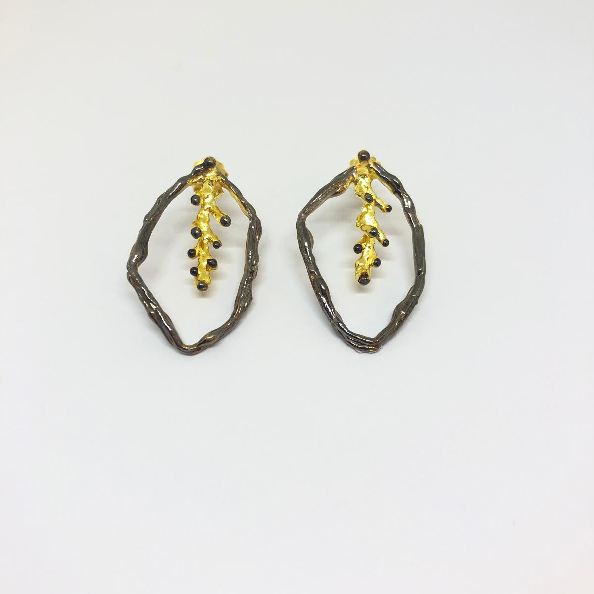 Front view of organic nature-inspired earrings. The botanical design showcases a striking contrast between the rustic blackened silver frame and the shining gold-plated inner branch details.