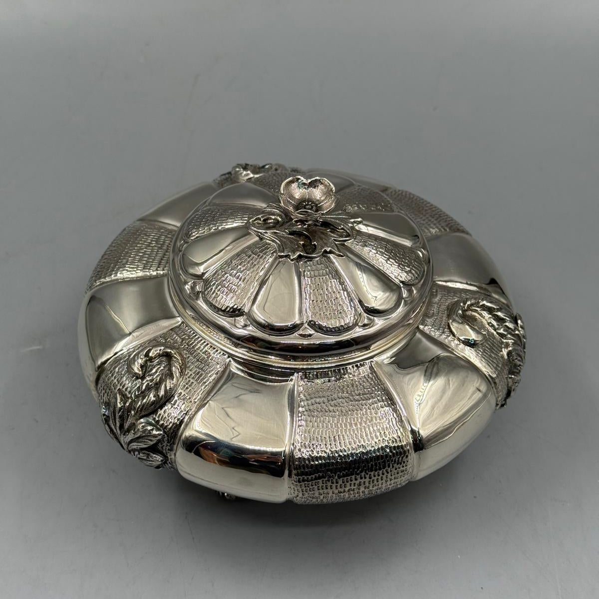 Top view of a vintage silver round box with ornate floral lid design.