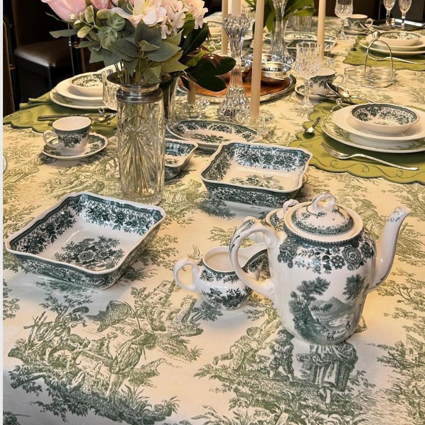 White tablecloth with green toile print draped over the table edge, highlighting the classic pattern and soft drape