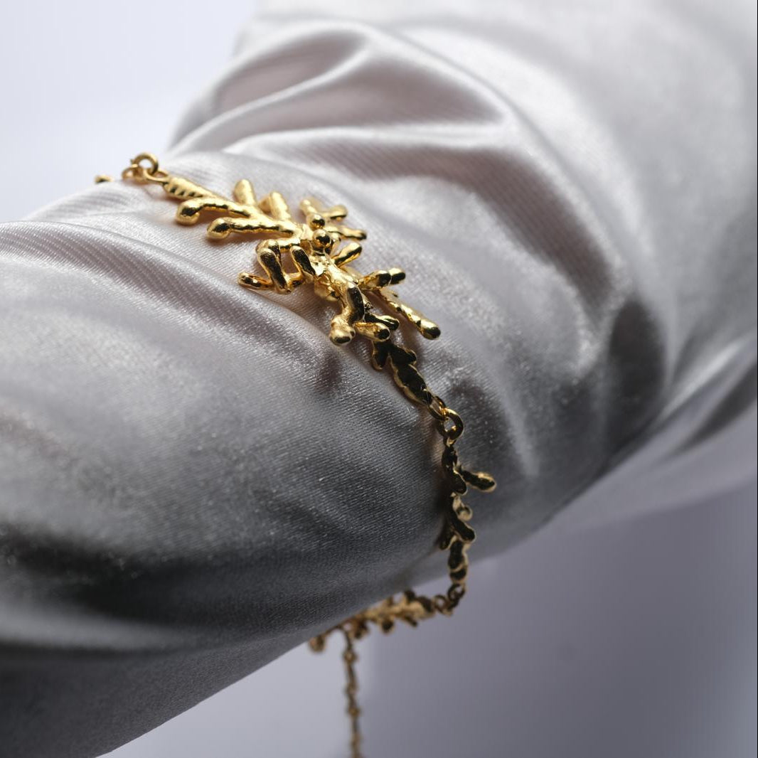 The complete 18K gold-plated pine branch bracelet laid out, showing the full design from the botanical links to the adjustable extension chain.